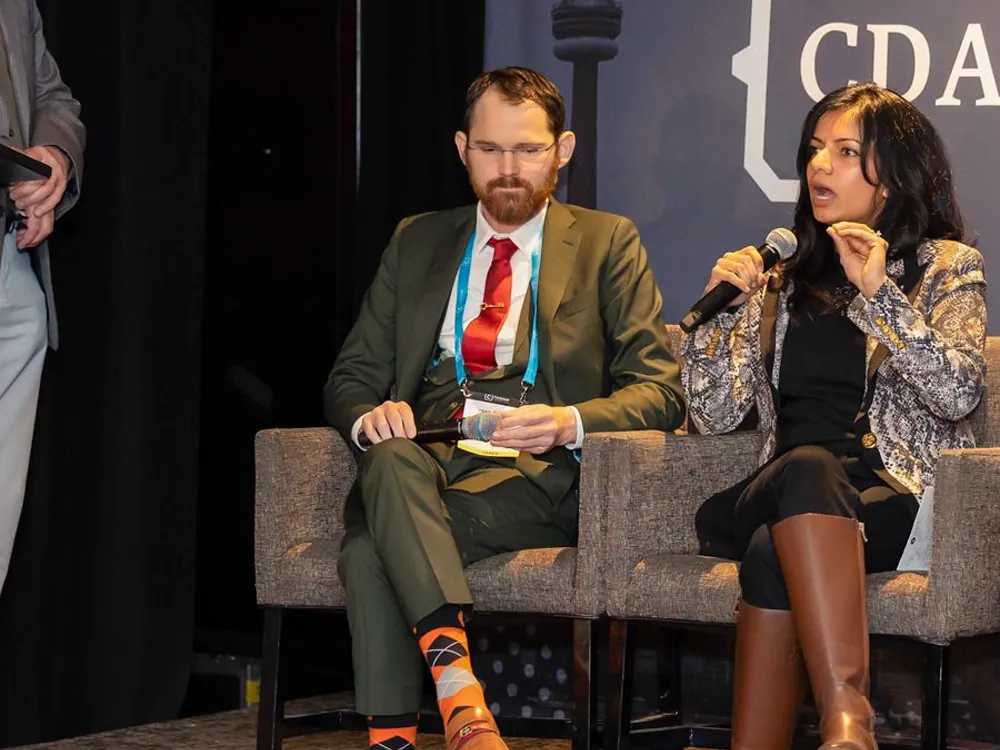 Seated on stage beside another panellist who is speaking into a microphone.
