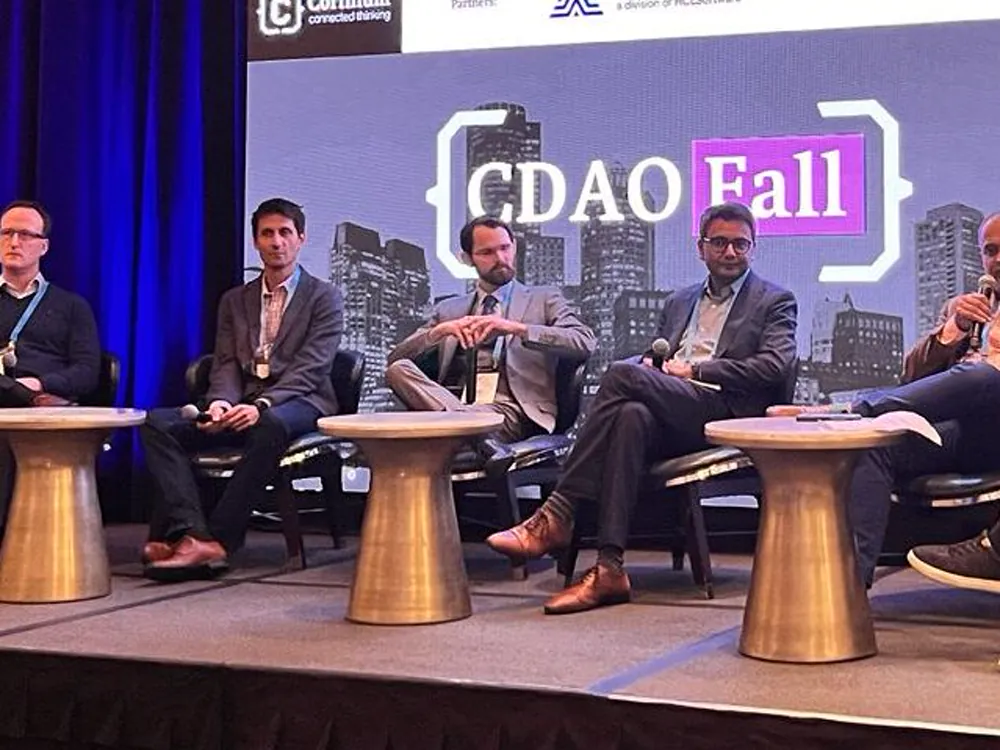 A panel of speakers seated on stage in front of a conference backdrop.